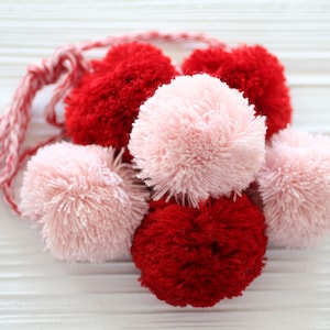 Könnte beinhalten: Eine Girlande aus roten und rosafarbenen, flauschigen Pompons, die mit einer rot-weißen Schnur zusammengebunden sind.