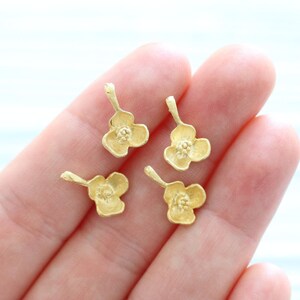 May include: Four gold-colored flower charms with a delicate design. Each charm has a small loop at the top for attaching to jewelry or other crafts.