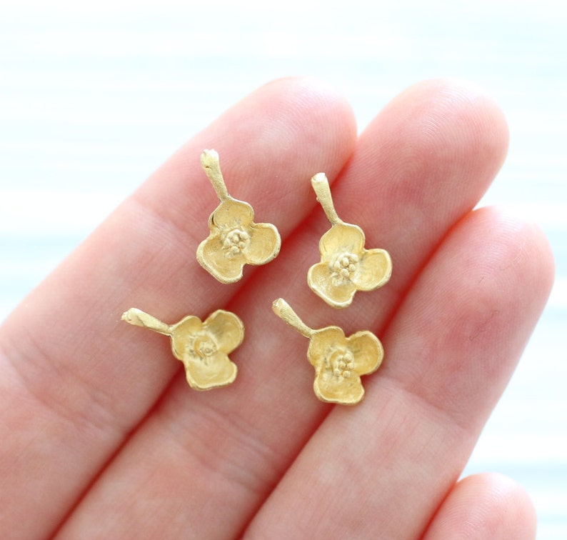 May include: Four gold-colored flower charms with a delicate design. Each charm has a small loop at the top for attaching to jewelry or other crafts.