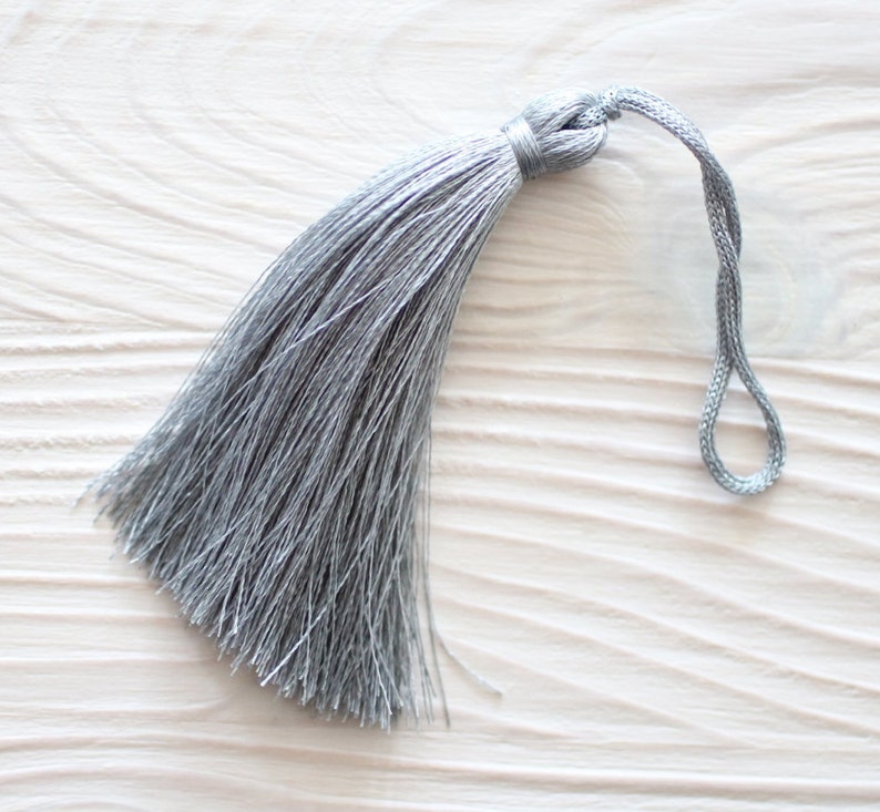 May include: A silver tassel with a long, thin fringe and a loop at the top.