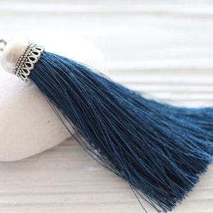 May include: A dark blue tassel with a silver metal top. The tassel is made of soft, thin threads and is about 6 inches long.