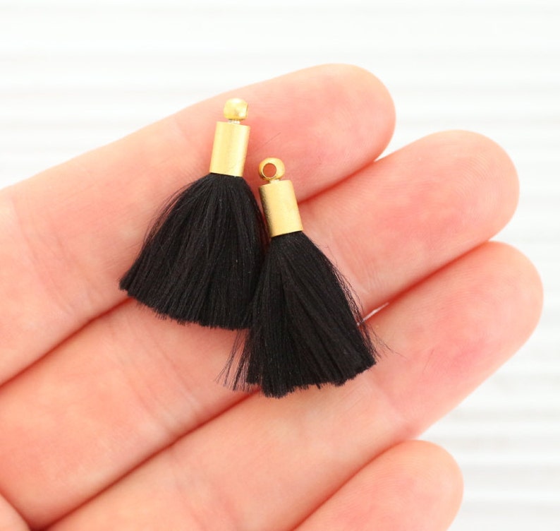 May include: Two black tassel trim with gold metal caps. The tassels are soft and fluffy.