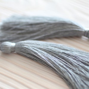 May include: Two gray tassel ornaments with a long, thin, fringed design. The tassels are made of soft, fluffy fibers and have a subtle sheen.