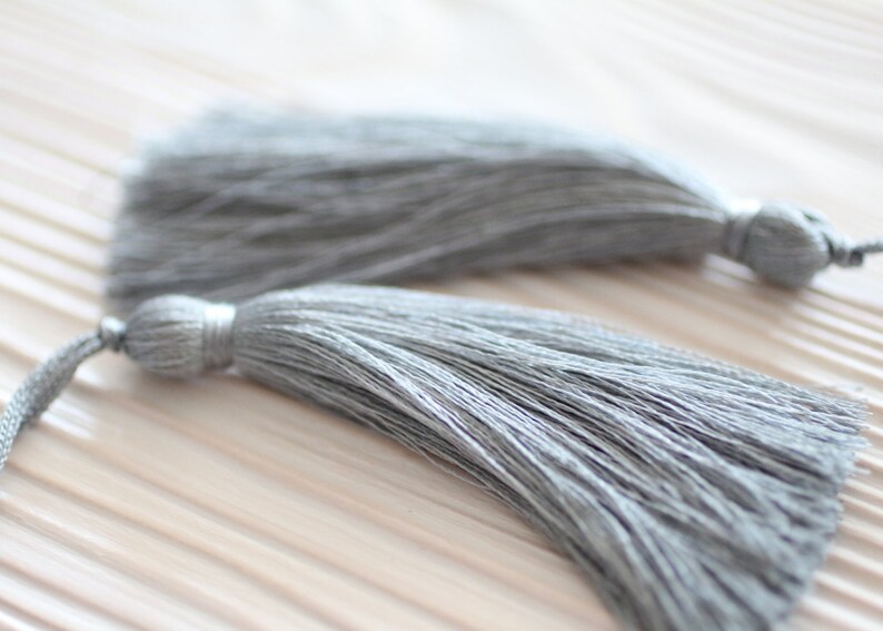 May include: Two gray tassel ornaments with a long, thin, fringed design. The tassels are made of soft, fluffy fibers and have a subtle sheen.