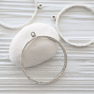 May include: Silver-toned metal circle pendants with a hammered texture. Each pendant has a small loop at the top for attaching to a chain or other jewelry component. The pendants are displayed on a white surface.
