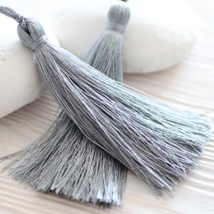 May include: Two silver gray tassel trims with a long, flowing fringe. The tassels are made of soft, silky threads and are perfect for adding a touch of elegance to any project.