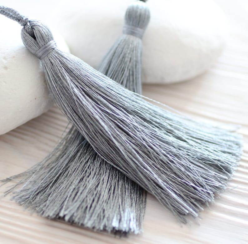 May include: Two silver gray tassel trims with a long, flowing fringe. The tassels are made of soft, silky threads and are perfect for adding a touch of elegance to any project.