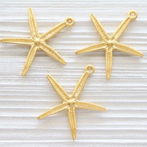 May include: Three gold-coloured starfish charms with a loop at the top for attaching to jewellery or other crafts.