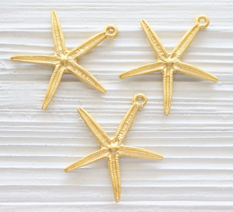 May include: Three gold-coloured starfish charms with a loop at the top for attaching to jewellery or other crafts.