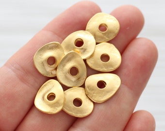 May include: A group of eight gold-toned metal beads with a slightly irregular, teardrop shape. Each bead has a round hole in the center.