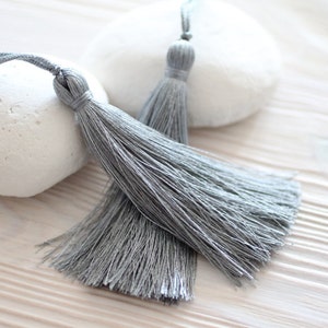 May include: Two gray tassel trim with a white background.