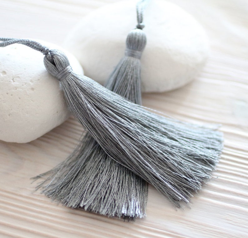 May include: Two gray tassel trim with a white background.
