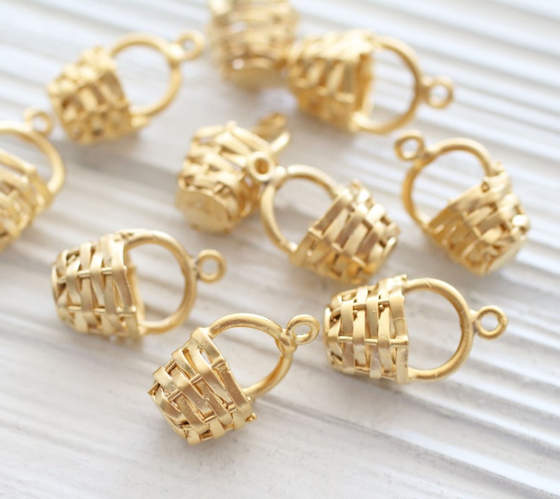 May include: A set of ten gold-toned metal basket charms with a woven design. The charms have a loop at the top for attaching to jewelry or other crafts.