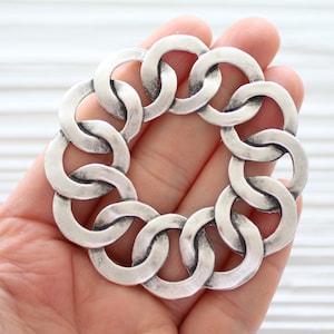 May include: Silver-toned metal chain link pendant with a circular shape. The pendant is made of multiple interconnected links, creating a decorative and intricate design.
