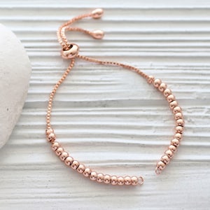 May include: A rose gold beaded bracelet with an adjustable sliding clasp. The bracelet is made of small, round beads and has a delicate, feminine look.