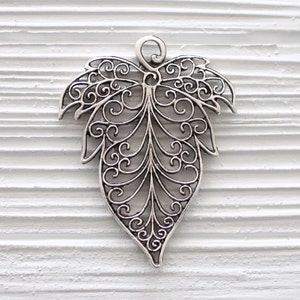 Op de afbeelding: Zilveren filigraan bladbedel met een delicaat, ingewikkeld ontwerp. De bedel is perfect om een ​​toets van elegantie toe te voegen aan sieraden of knutselwerk.