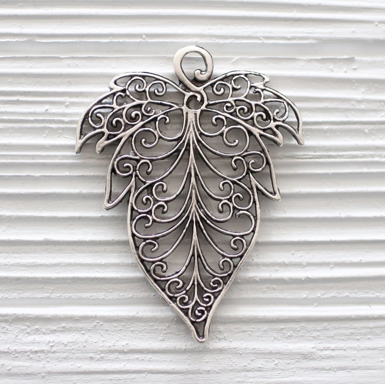 Op de afbeelding: Zilveren filigraan bladbedel met een delicaat, ingewikkeld ontwerp. De bedel is perfect om een ​​toets van elegantie toe te voegen aan sieraden of knutselwerk.