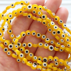 Op de afbeelding: Een streng gele glazen kralen met een wit en zwart boze oog ontwerp.