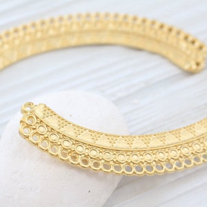 May include: Gold-toned metal jewelry component with a decorative, intricate design. The component is shaped like a half-circle and has a scalloped edge.