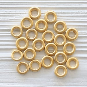 Op de afbeelding: Een verzameling van 20 gouden metalen springringen, losjes gerangschikt op een wit houten oppervlak.
