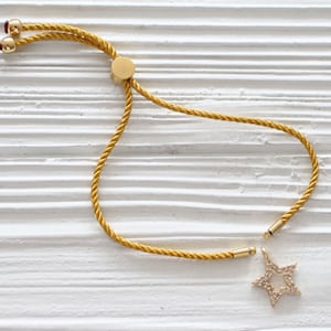 May include: A yellow cord bracelet with a gold star charm. The star is encrusted with small clear stones.