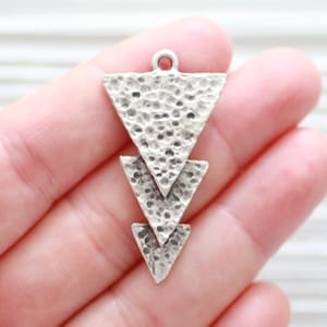 May include: Silver pendant charm with three layered triangle shapes. Each triangle has a textured surface.
