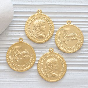 May include: Four gold-colored metal coin charms with Roman emperor busts and inscriptions. The charms feature a profile of a man with a laurel wreath and the inscription "IMP ANTONINVS PIVS AVG".