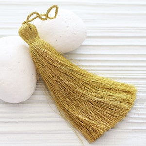 May include: A gold tassel with a metallic sheen, hanging from a white surface.