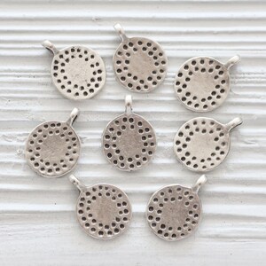 Peut inclure: Huit breloques rondes en m&eacute;tal argent&eacute; avec un motif circulaire d&eacute;coratif. Chaque breloque a une petite boucle en haut pour l'attacher &agrave; des bijoux ou d'autres objets artisanaux.