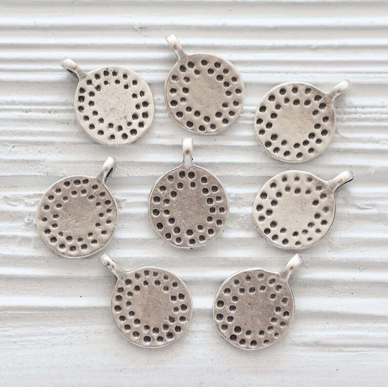Peut inclure: Huit breloques rondes en m&eacute;tal argent&eacute; avec un motif circulaire d&eacute;coratif. Chaque breloque a une petite boucle en haut pour l'attacher &agrave; des bijoux ou d'autres objets artisanaux.