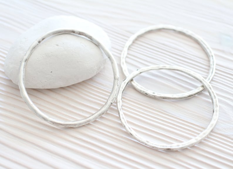 Puede incluir: Tres pulseras de plata con textura martillada. Las pulseras est&aacute;n apiladas una encima de la otra.