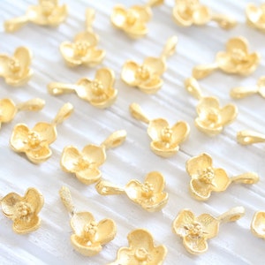 May include: A collection of gold-colored metal flower charms with a delicate design. The charms are perfect for jewelry making, scrapbooking, and other craft projects.