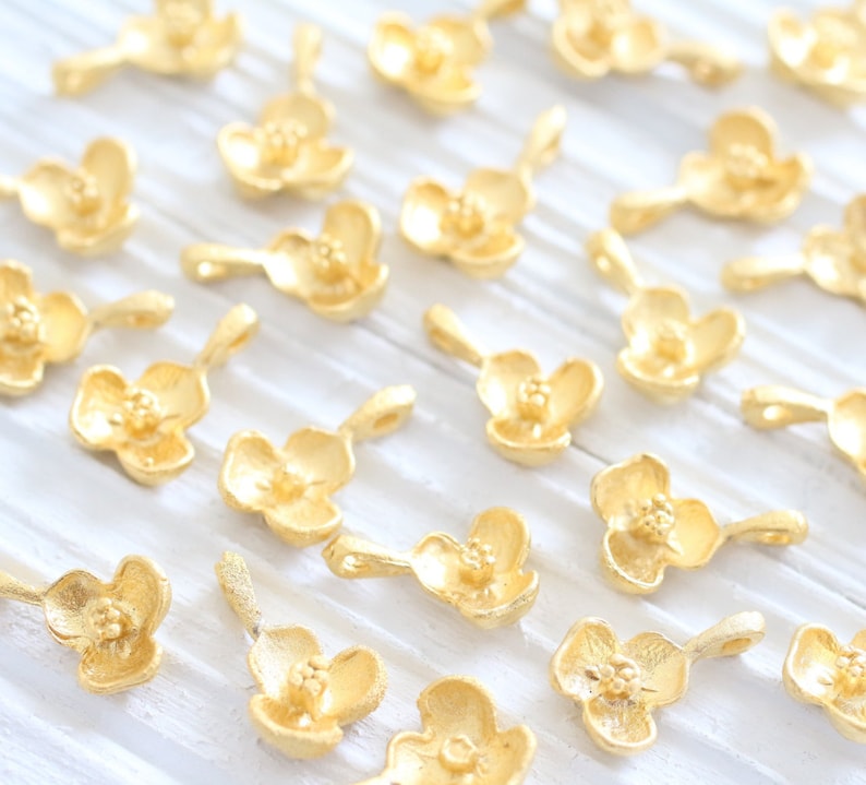 May include: A collection of gold-colored metal flower charms with a delicate design. The charms are perfect for jewelry making, scrapbooking, and other craft projects.