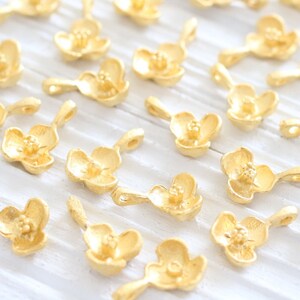 May include: A collection of gold-toned metal charms shaped like delicate flowers. Each charm has a small loop for attaching to jewelry or other crafts.