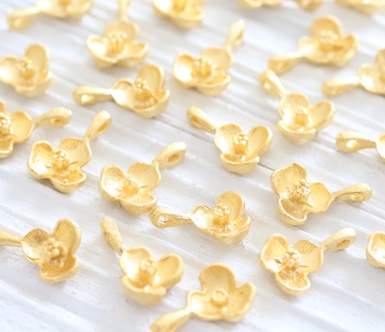 May include: A collection of gold-toned metal charms shaped like delicate flowers. Each charm has a small loop for attaching to jewelry or other crafts.