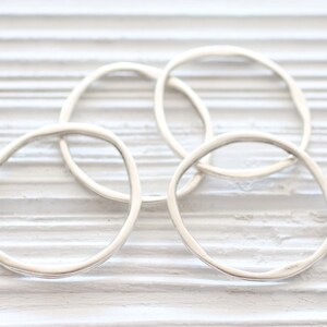 May include: Four silver rings, each with a slightly different shape, are stacked on a white wooden surface. The rings are all smooth and shiny.