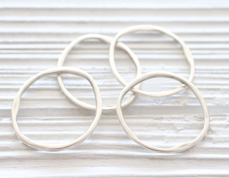 May include: Four silver rings, each with a slightly different shape, are stacked on a white wooden surface. The rings are all smooth and shiny.