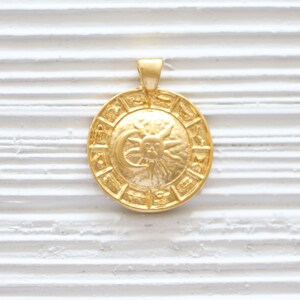 Puede incluir: Colgante dorado con un dise&ntilde;o circular con los signos del zod&iacute;aco y un gr&aacute;fico de sol y luna.