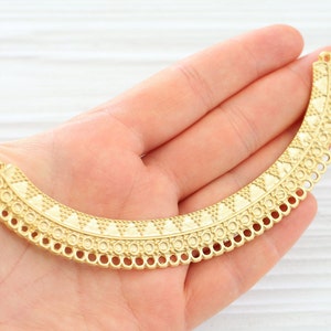 May include: Gold-toned metal jewelry connector with a decorative, scalloped edge and a geometric pattern.