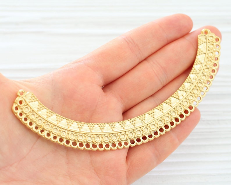 May include: Gold-toned metal jewelry connector with a decorative, scalloped edge and a geometric pattern.