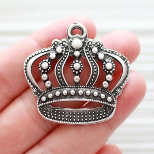 May include: Silver crown charm with a detailed design, featuring a loop at the top for hanging.