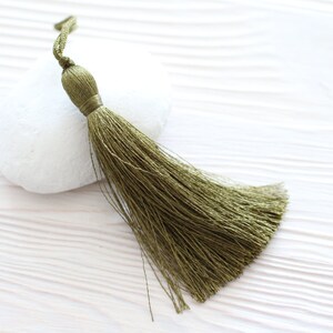 May include: A green tassel with a long, flowing fringe. The tassel is made of soft, silky threads and has a knotted top.