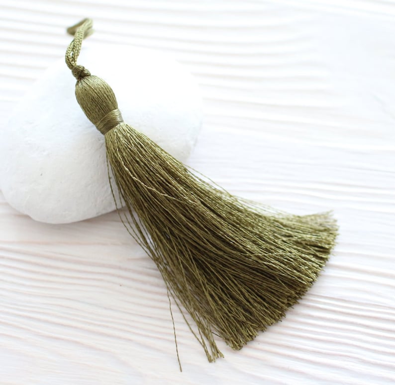 May include: A green tassel with a long, flowing fringe. The tassel is made of soft, silky threads and has a knotted top.
