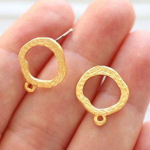 May include: A pair of gold-toned earring blanks with a textured, irregular oval shape and a jump ring at the bottom.