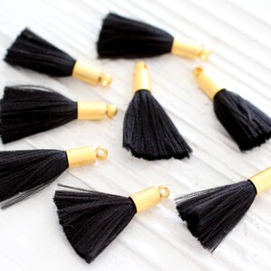 May include: Eight black tassels with gold metal caps. The tassels are made of soft, fluffy fibers and are perfect for adding a touch of elegance to any project.