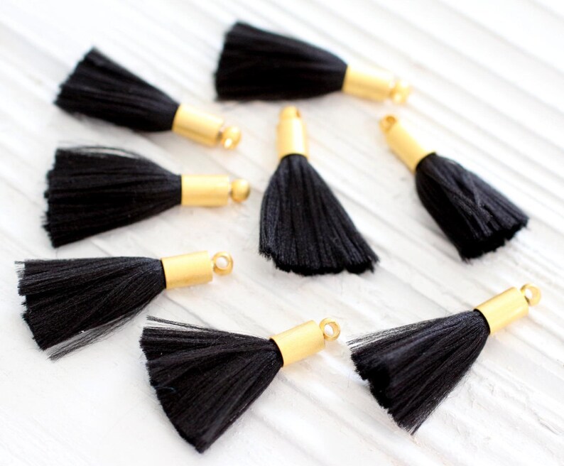 May include: Eight black tassels with gold metal caps. The tassels are made of soft, fluffy fibers and are perfect for adding a touch of elegance to any project.