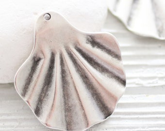 May include: A silver-toned metal seashell charm with a textured surface. The charm has a hole at the top for attaching to jewelry or other crafts.