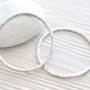 Puede incluir: Dos pulseras de plata martilladas sobre una superficie de madera blanca.