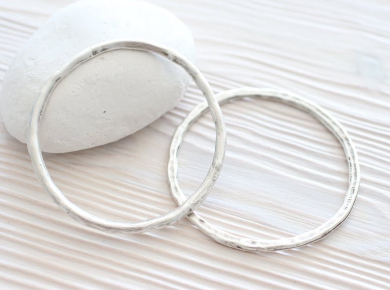 Puede incluir: Dos pulseras de plata martilladas sobre una superficie de madera blanca.