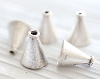 May include: Five silver cone-shaped metal beads with a hole at the top. The beads are arranged on a white surface.